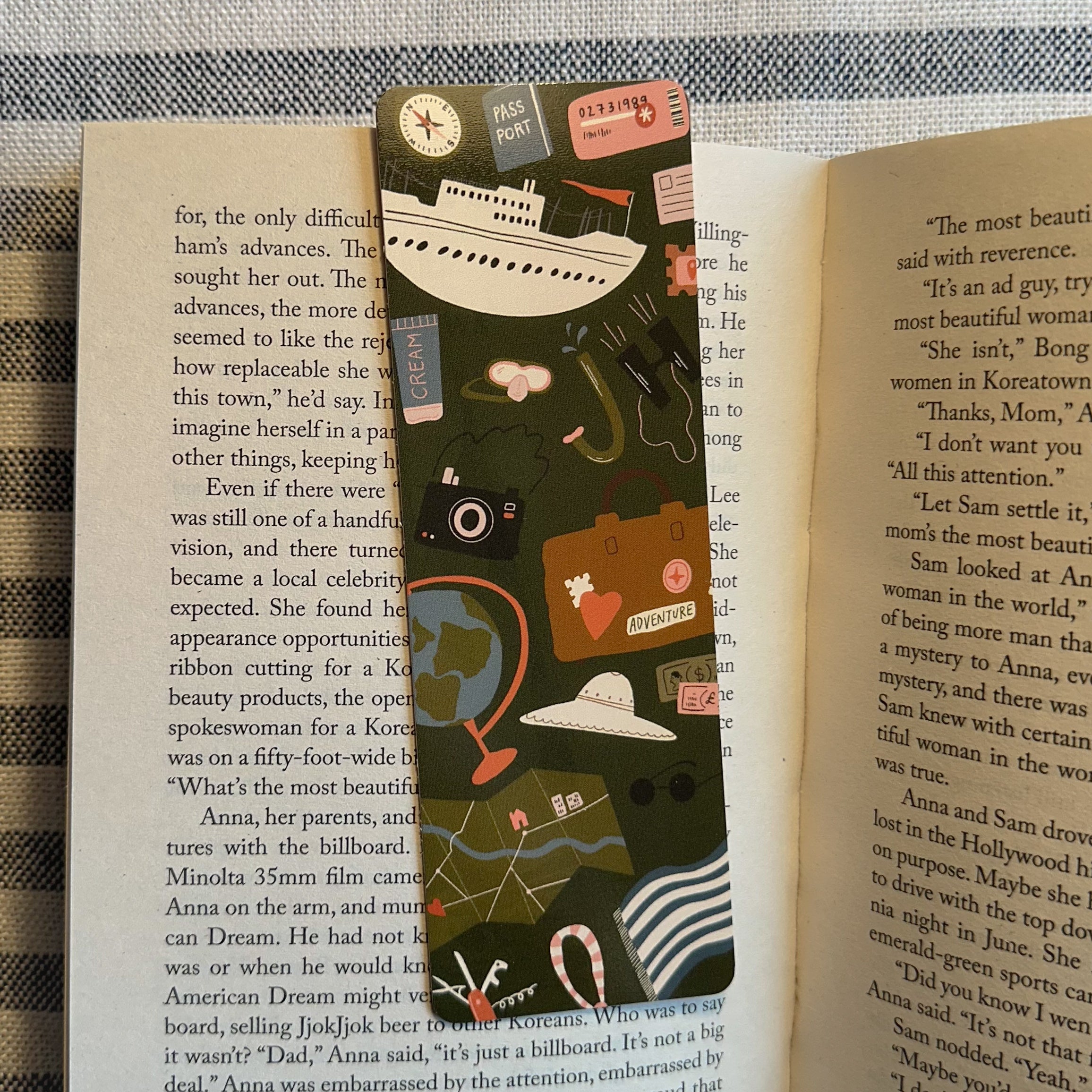 A double-sided travel-themed bookmark with illustrations of travel-related items like a ship, plane, and camera, placed vertically inside an open book.